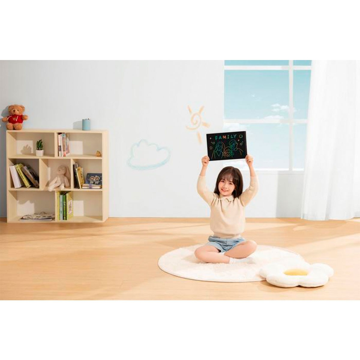 Mała dziewczynka siedzi trzymając czarny tablet. Jest na dywanie z poduszką w kształcie misia.