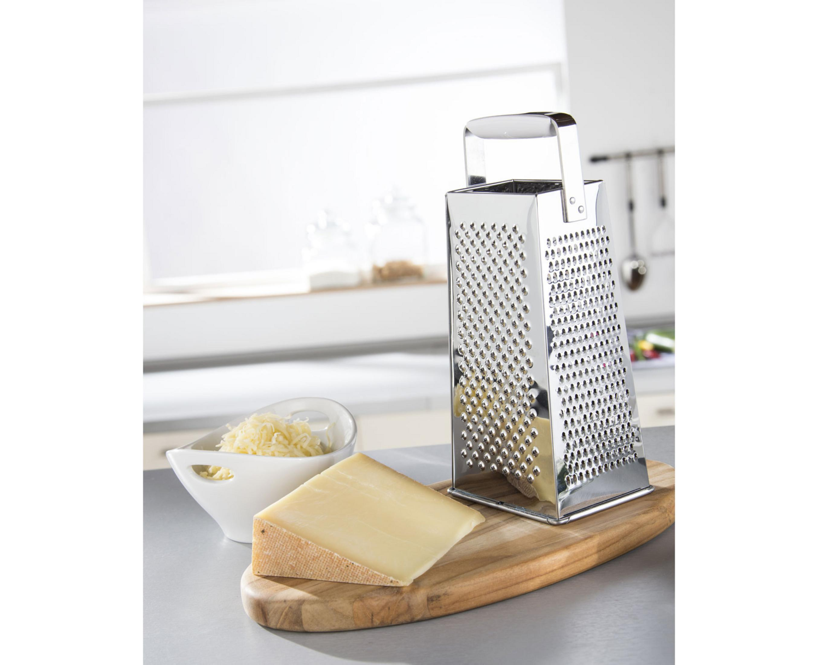 Eine Käse reibe steht neben einem Käse Keil und einer Schüssel mit geriebenem Käse auf einem Holzbrett.