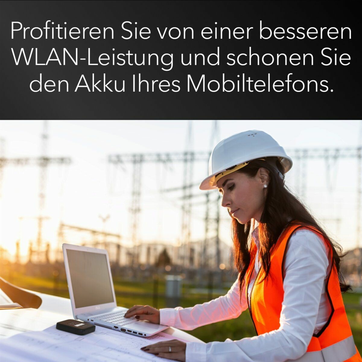 Una donna con casco e giubbotto arancione lavora su un laptop con un router wifi su una superficie.