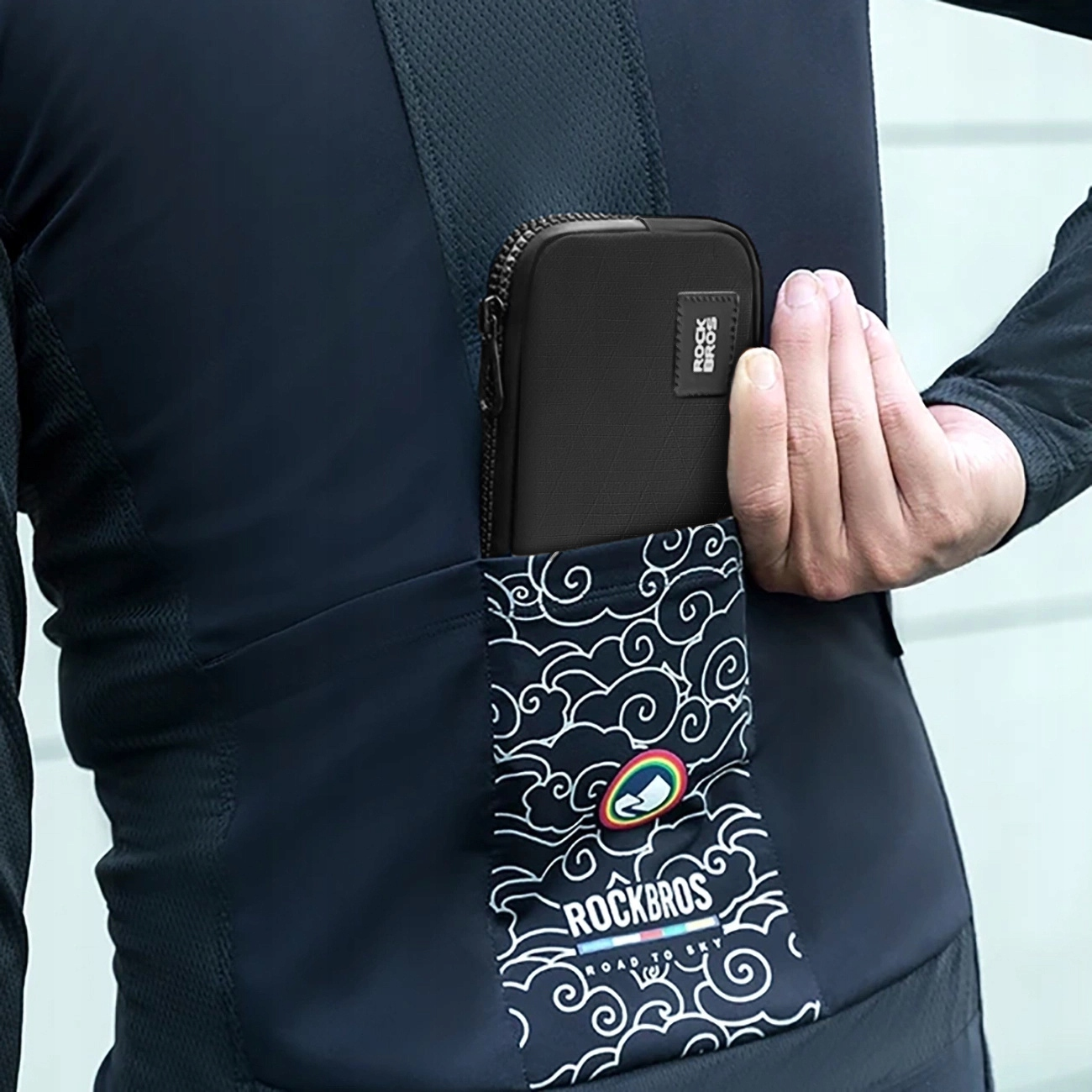 Osoba w czarnej koszulce kolarskiej ma czarne etui na telefon w kieszeni z wzorem chmur i logo Rockbros.