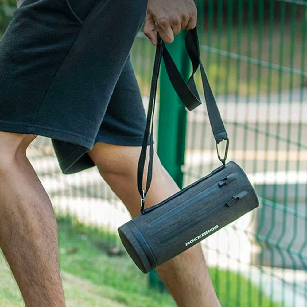 Osoba niesie szarą, cylindryczną torbę z czarnym paskiem. Na torbie napis 'ROCKBROS'.