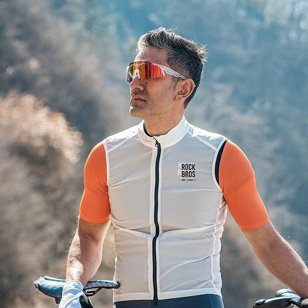 Mężczyzna w białej kamizelce i pomarańczowych rękawach w okularach przeciwsłonecznych. Stoi na zewnątrz z niebieskim tłem.