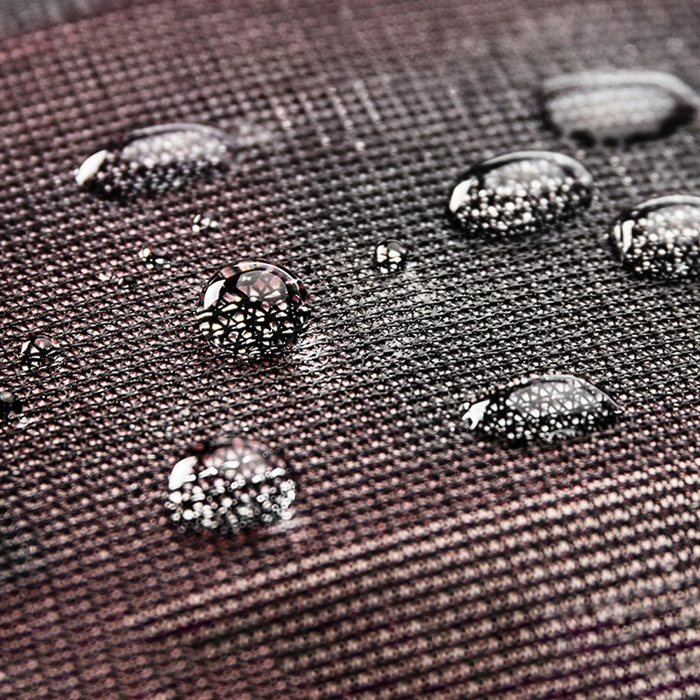 Zbliżenie kropli wody na ciemnej, teksturowanej tkaninie, tworzących powierzchnię odbijającą światło.