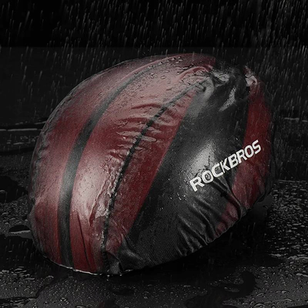 Kask rowerowy pokryty osłoną przeciwdeszczową z napisem 'ROCKBROS'. Pada deszcz.