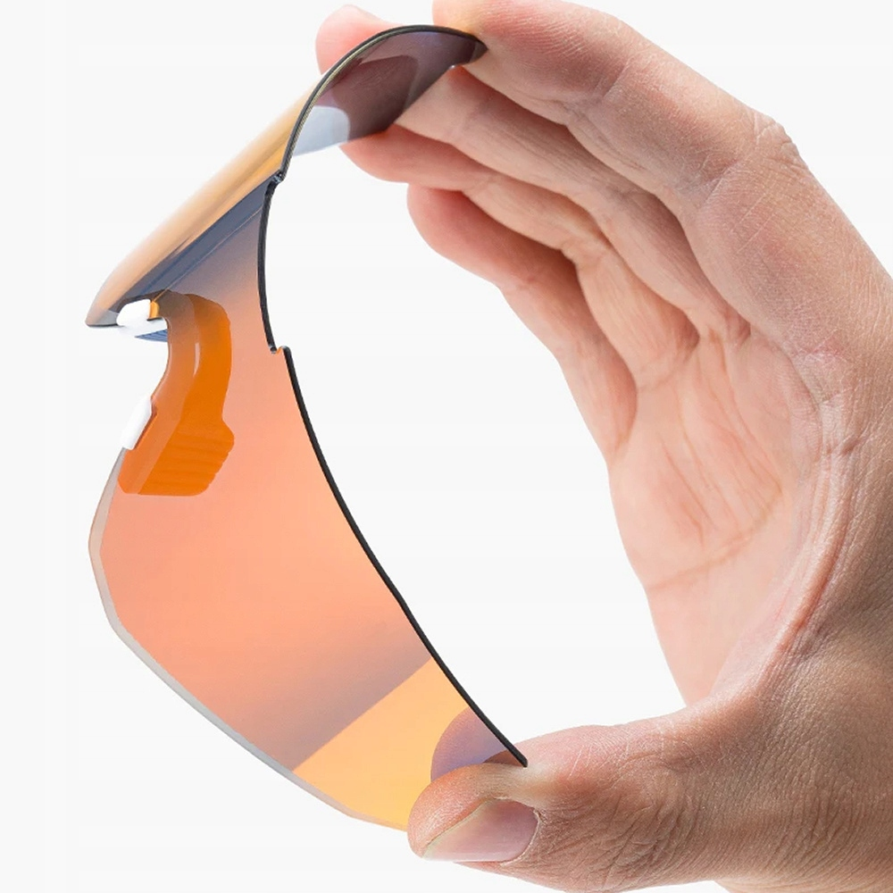 Dłoń trzymająca pomarańczową soczewkę okularów przeciwsłonecznych. Soczewka jest lekko zgięta.
