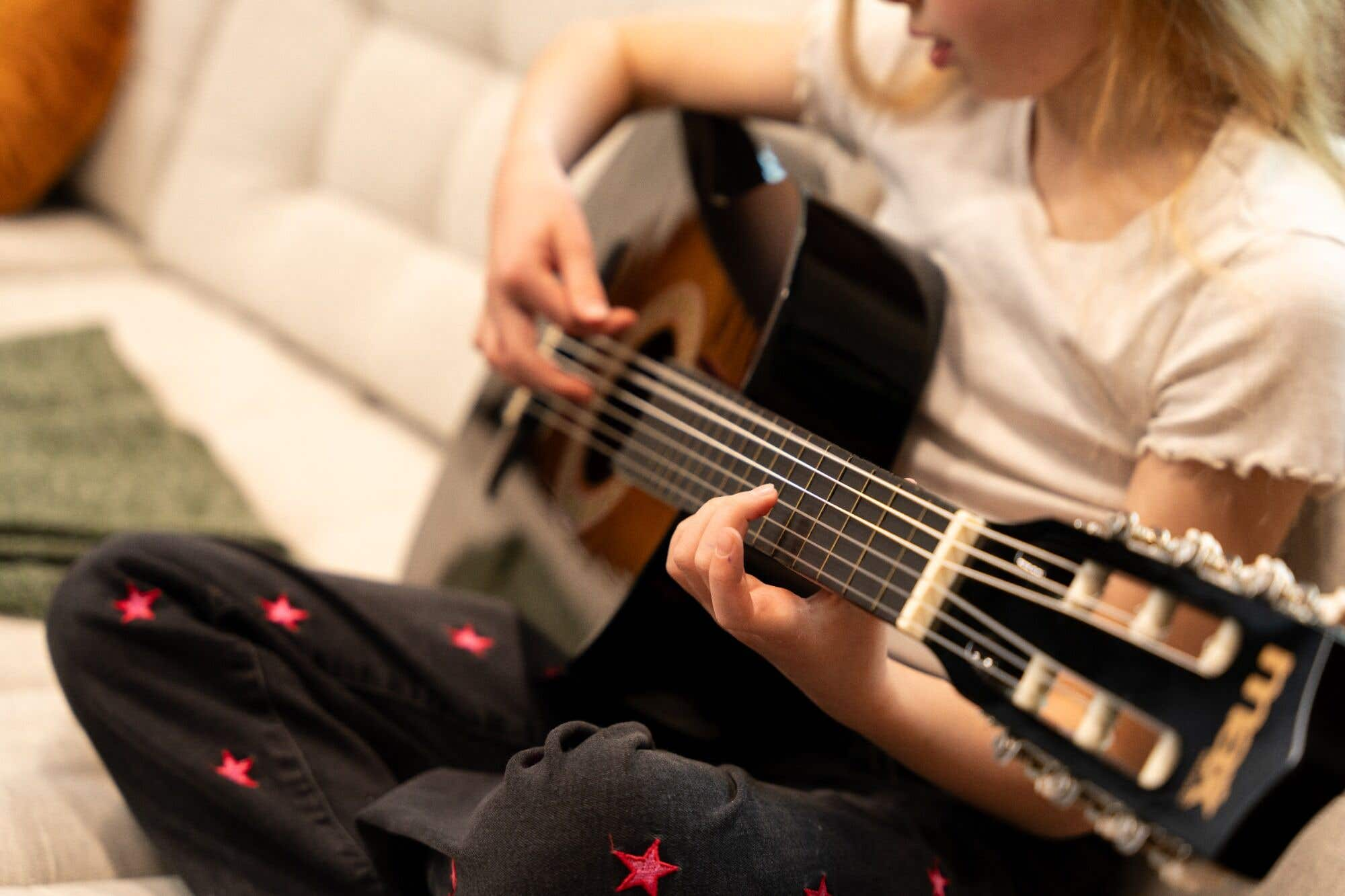Primer plano de niña tocando guitarra, con jeans de estrellas, sujetando el mástil.