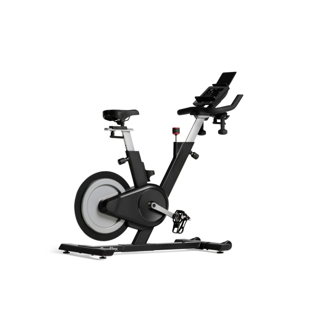 Una bicicleta estática en un estudio, negra y gris, con una pantalla digital.