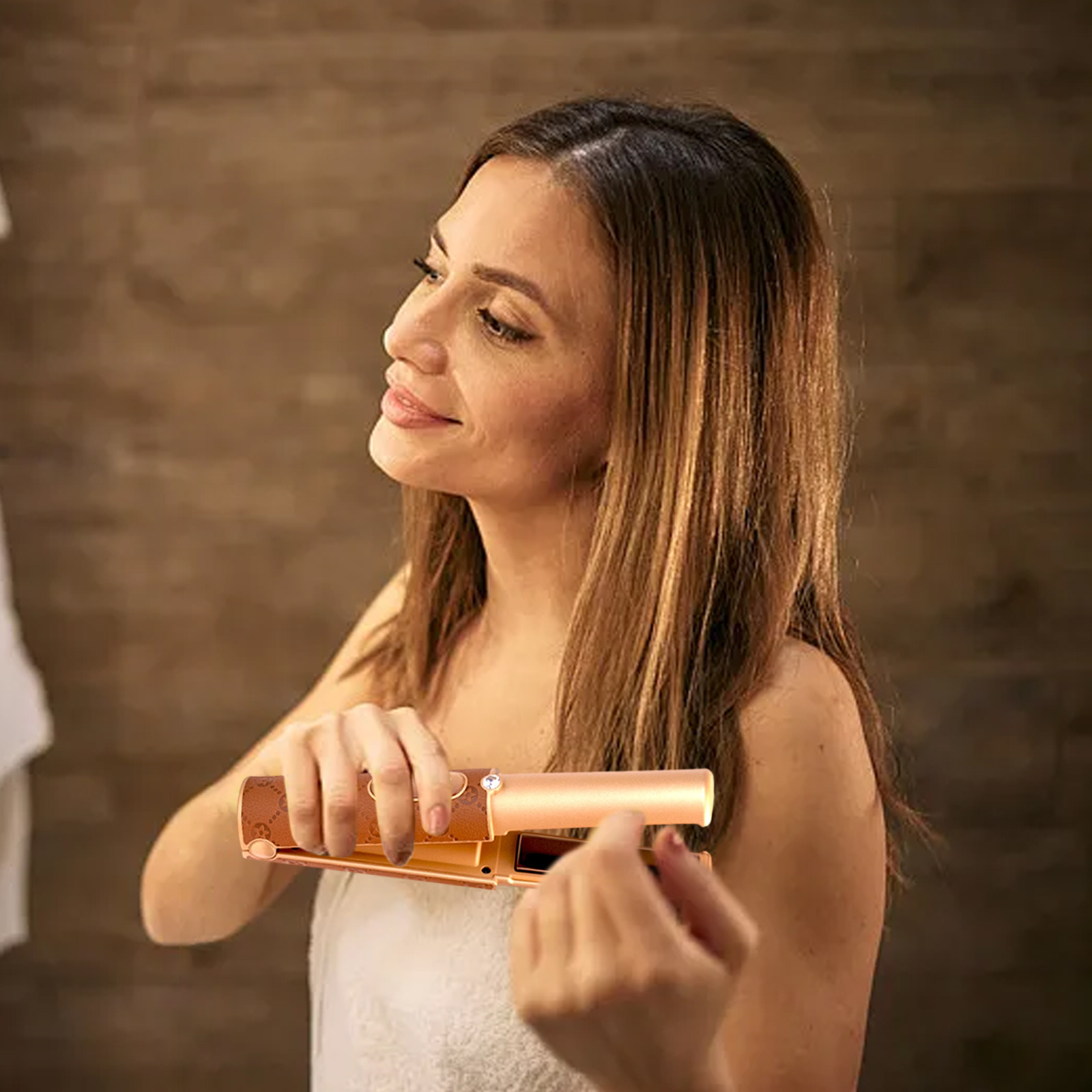 Frau im Handtuch benutzt einen Haarglätter im Badezimmer. Der Glätter ist braun und gold.