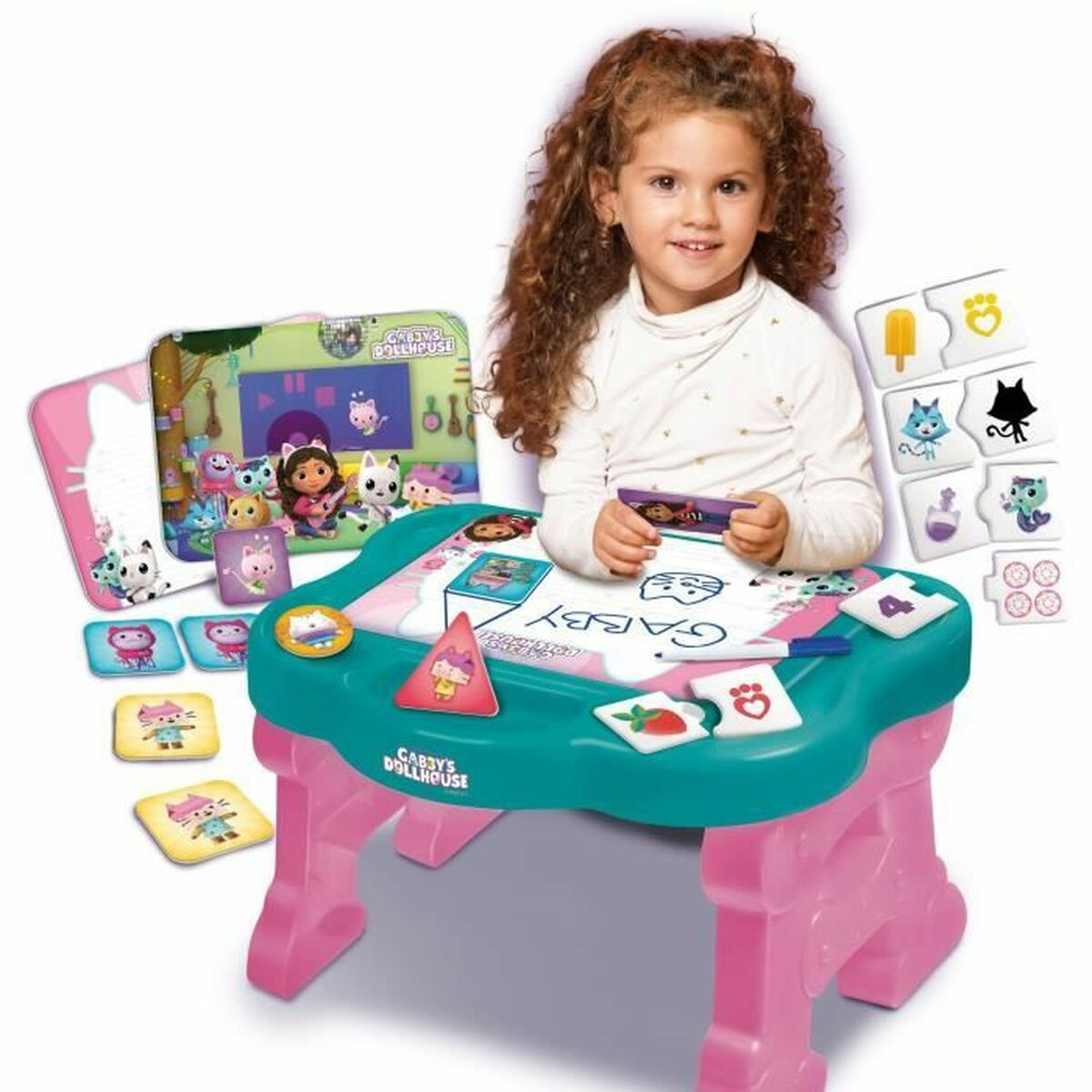 Una ragazzina siede a una scrivania giocattolo, circondata da personaggi giocattolo e da una scatola della Gabby's Dollhouse.