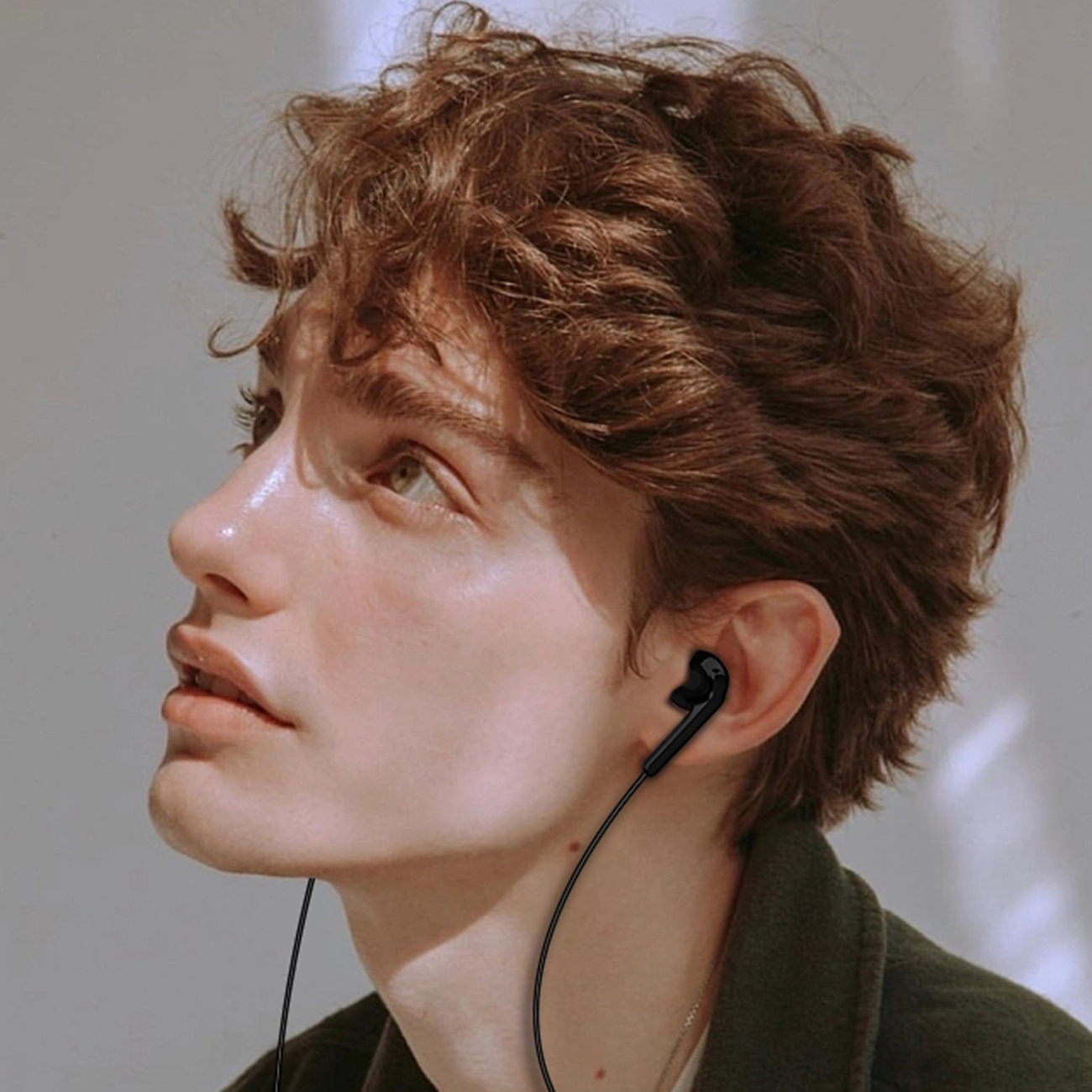 Una persona con i capelli castani che indossa auricolari, che guarda in alto a sinistra.