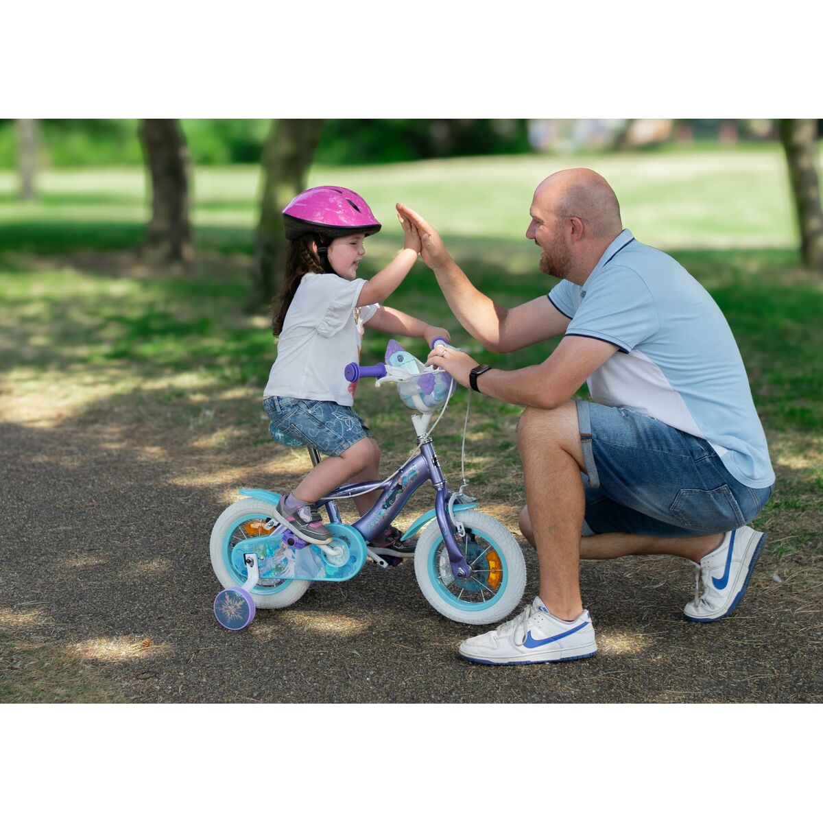 Ein Mädchen auf einem Fahrrad gibt einem Mann im Park High-Five. Das Fahrrad hat Stützräder.