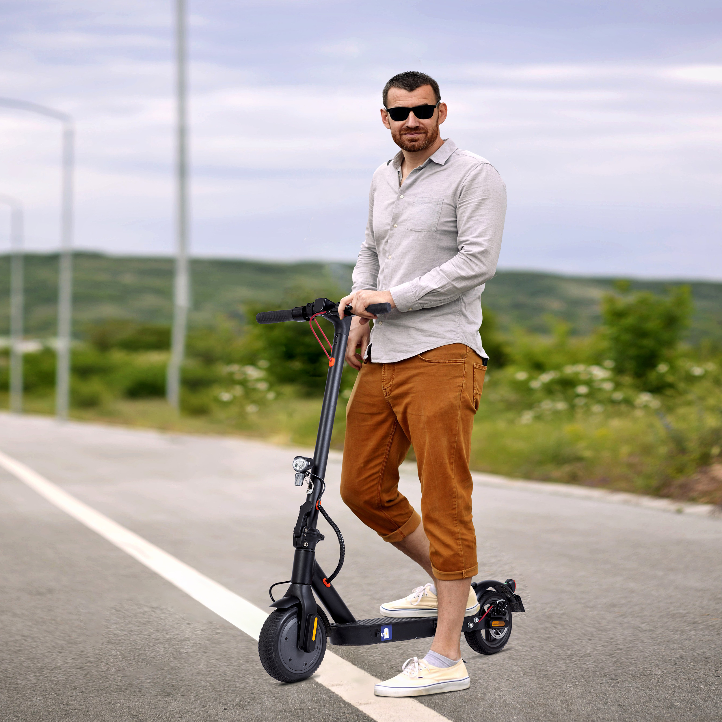 Mężczyzna w okularach przeciwsłonecznych stoi na drodze z hulajnogą elektryczną, trzymając kierownicę.