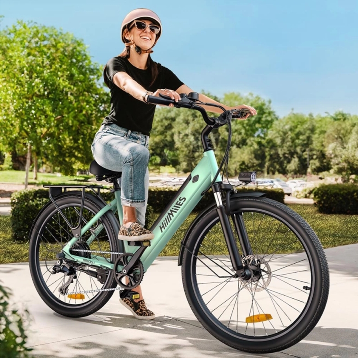 Una donna guida una bici elettrica verde menta in una giornata di sole. Indossa un casco e jeans.