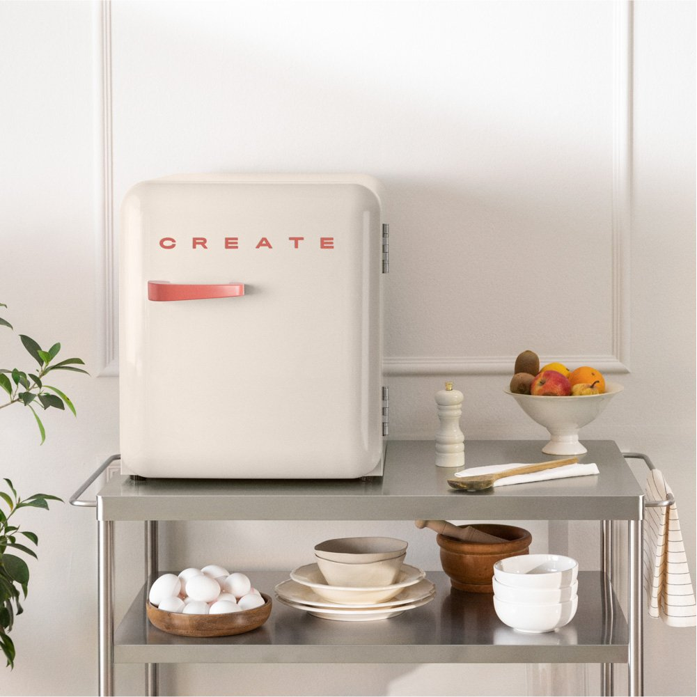 Mini nevera color crema con asa roja, texto "CREATE", ambiente de cocina.