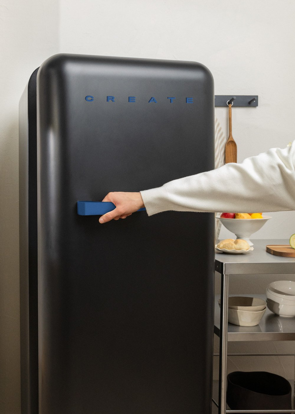 Persona abriendo nevera alta negra con asa azul, ambiente de cocina.
