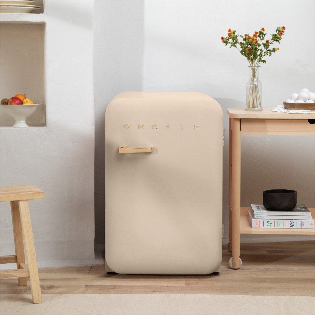 Nevera beige con la palabra 'CREATE'. Son visibles un jarrón con flores y un taburete de madera.