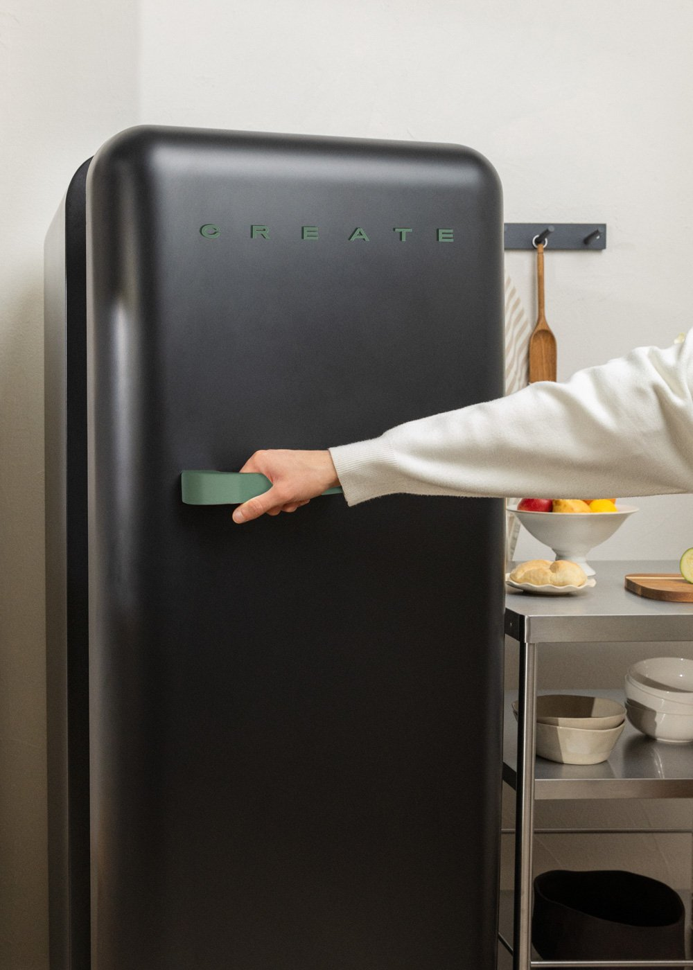 Una mano abre una nevera negra con la palabra 'CREATE' en verde. Es visible una estantería con comida.