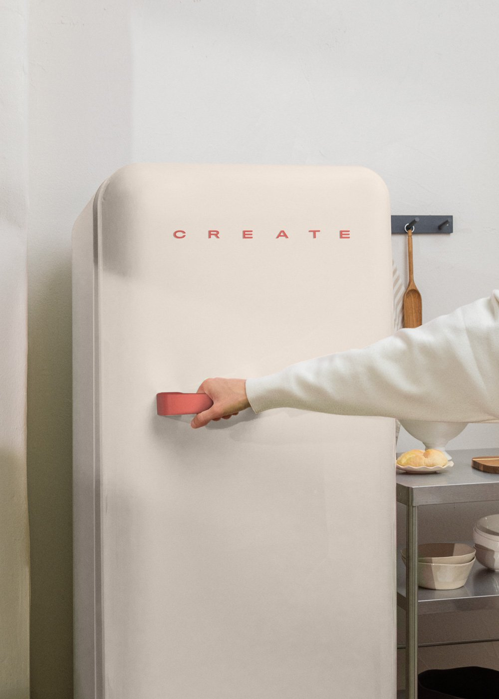 Una mano abre un refrigerador crema con manija rosa. CREATE en la puerta. Carrito con comida cerca.