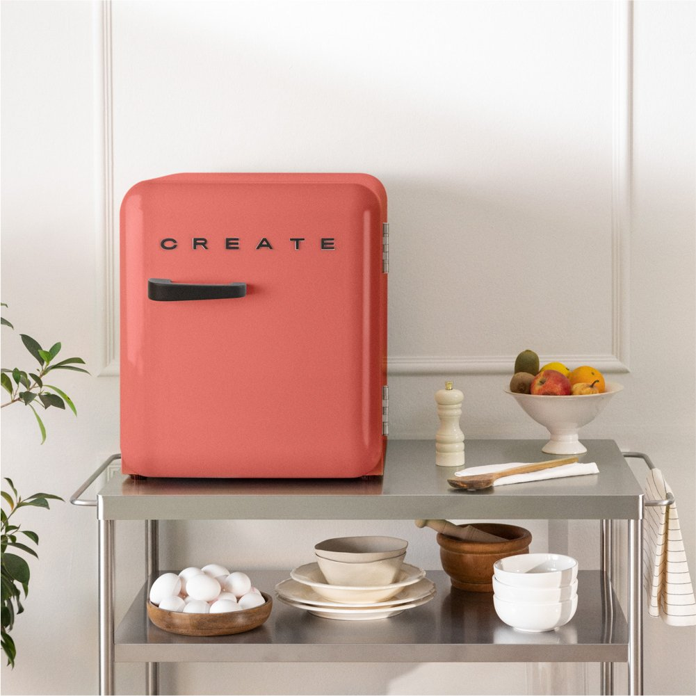 Un mini-refrigerador coral con CREATE sobre un carrito de metal con huevos y fruta.