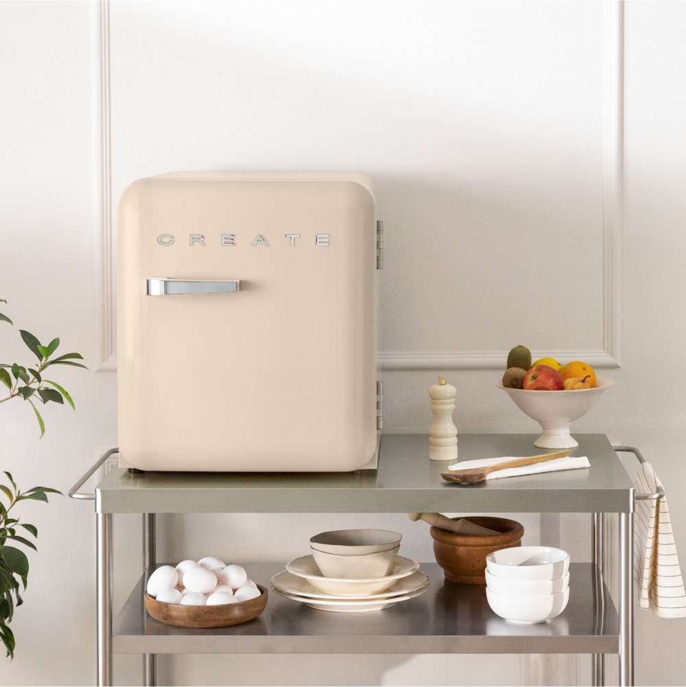 Un mini-refrigerador beige con CREATE sobre un carrito de metal con huevos y fruta.