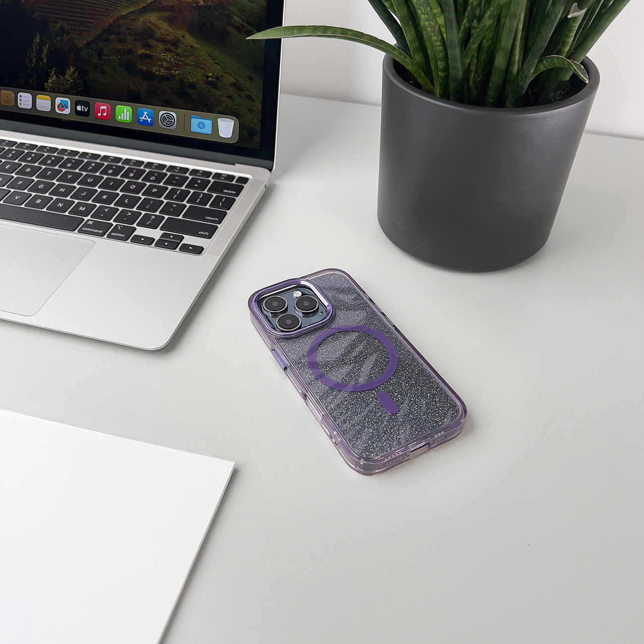 Etui na telefon na białym biurku. Etui na telefon leży na białym biurku obok laptopa i rośliny.