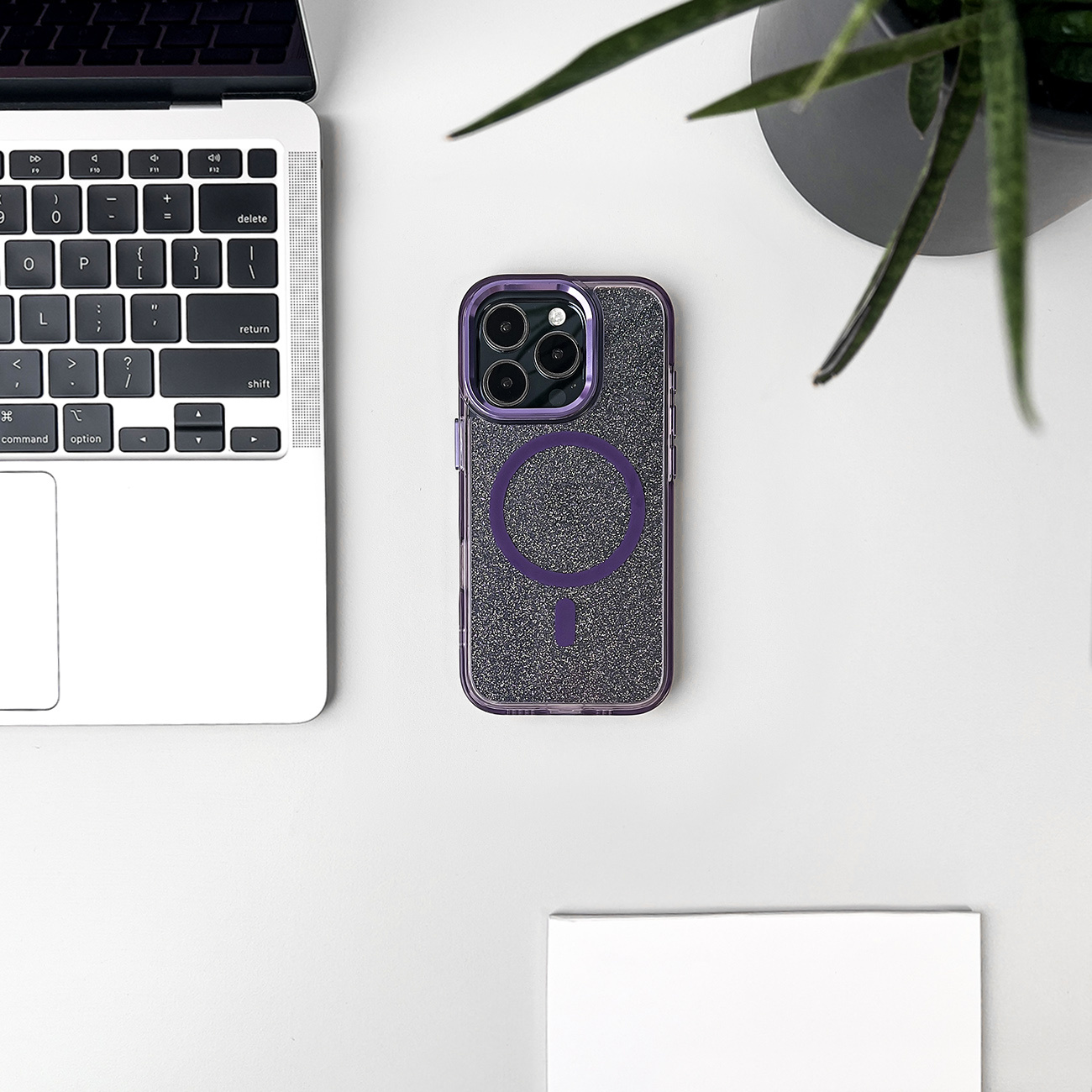 Etui na telefon na białym biurku. Etui na telefon leży na białym biurku obok laptopa i rośliny.