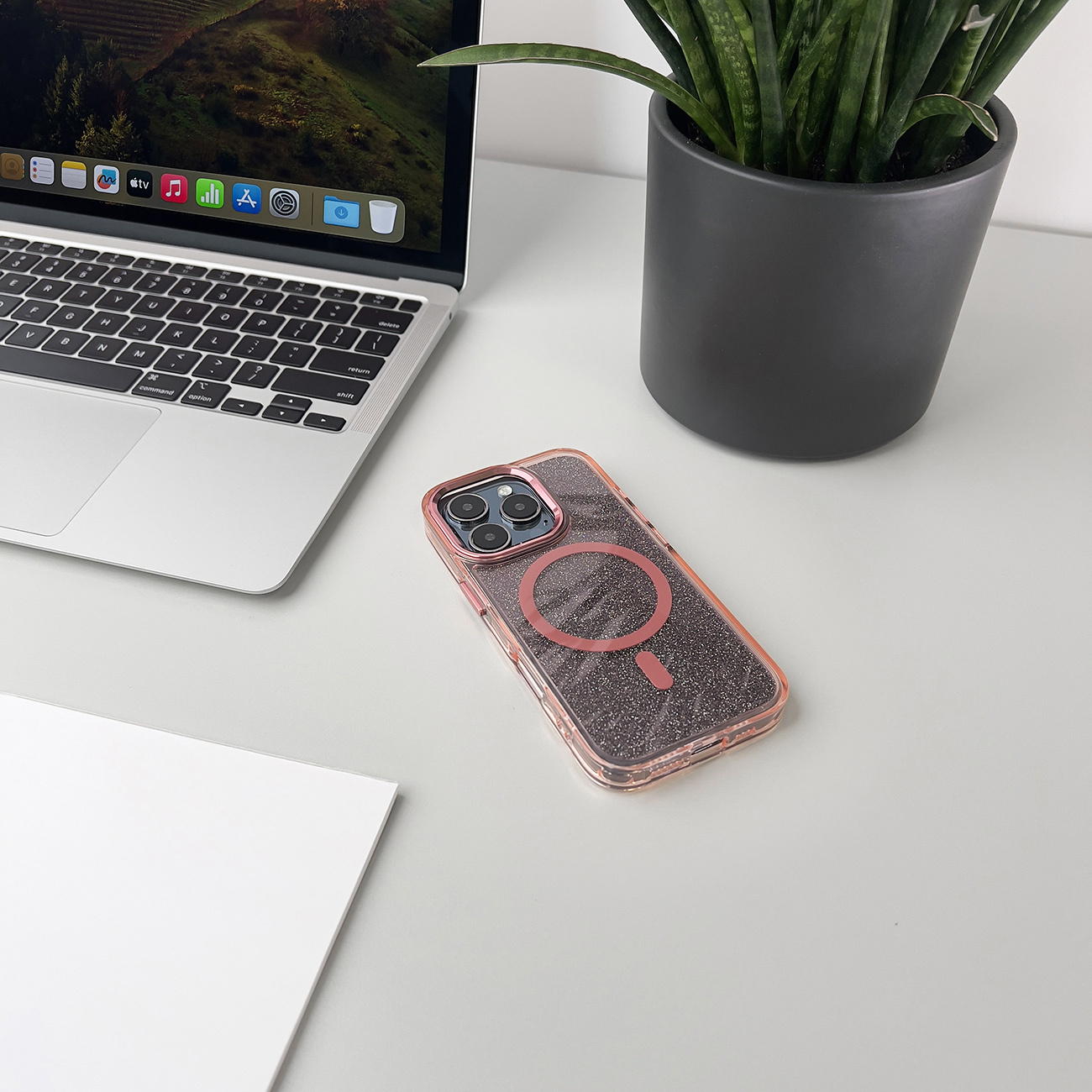 Etui na telefon na biurku, z laptopem i rośliną. Etui różowe i ma magnetyczny okrąg.