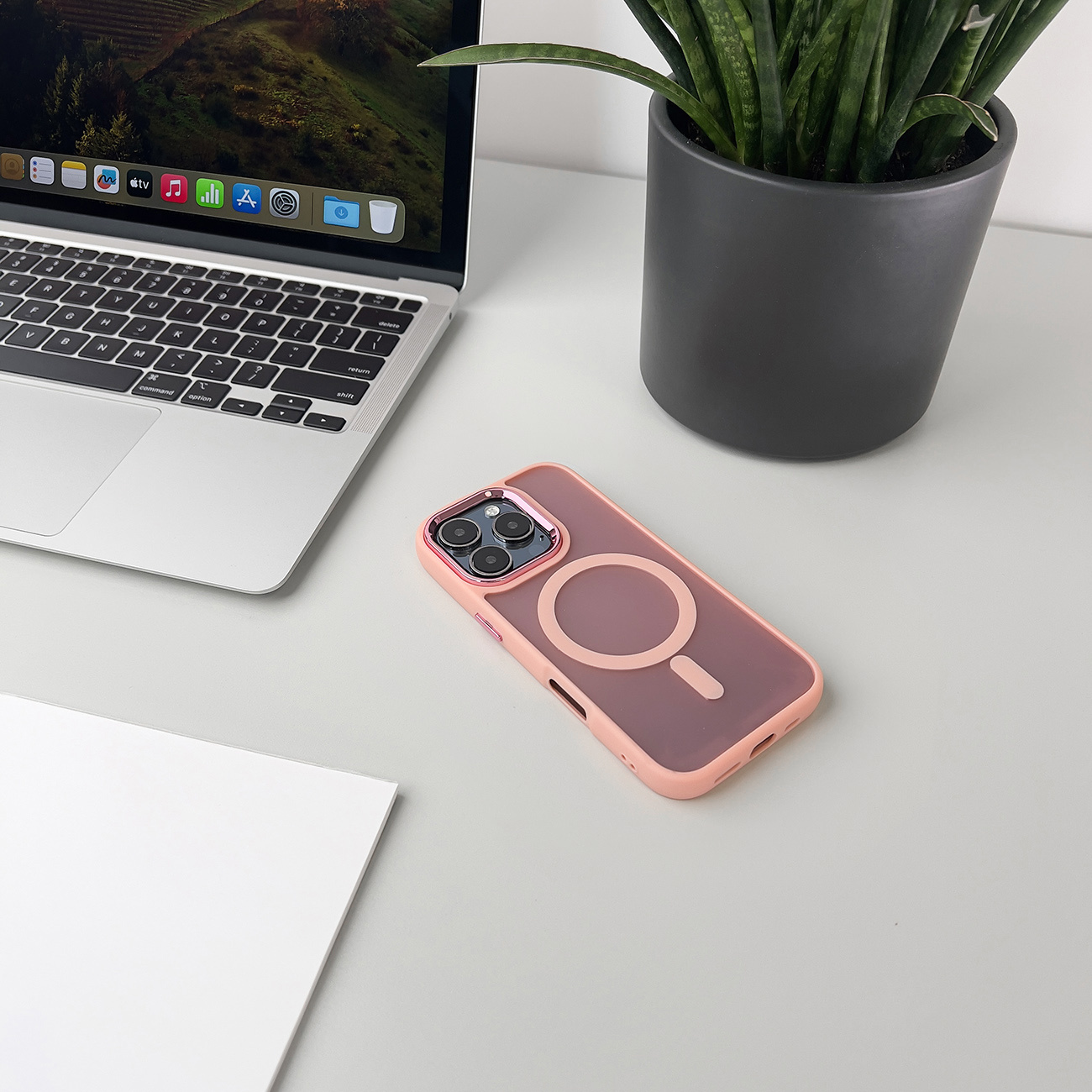 Etui na telefon na biurku, z laptopem i rośliną. Etui różowe i ma magnetyczny okrąg.
