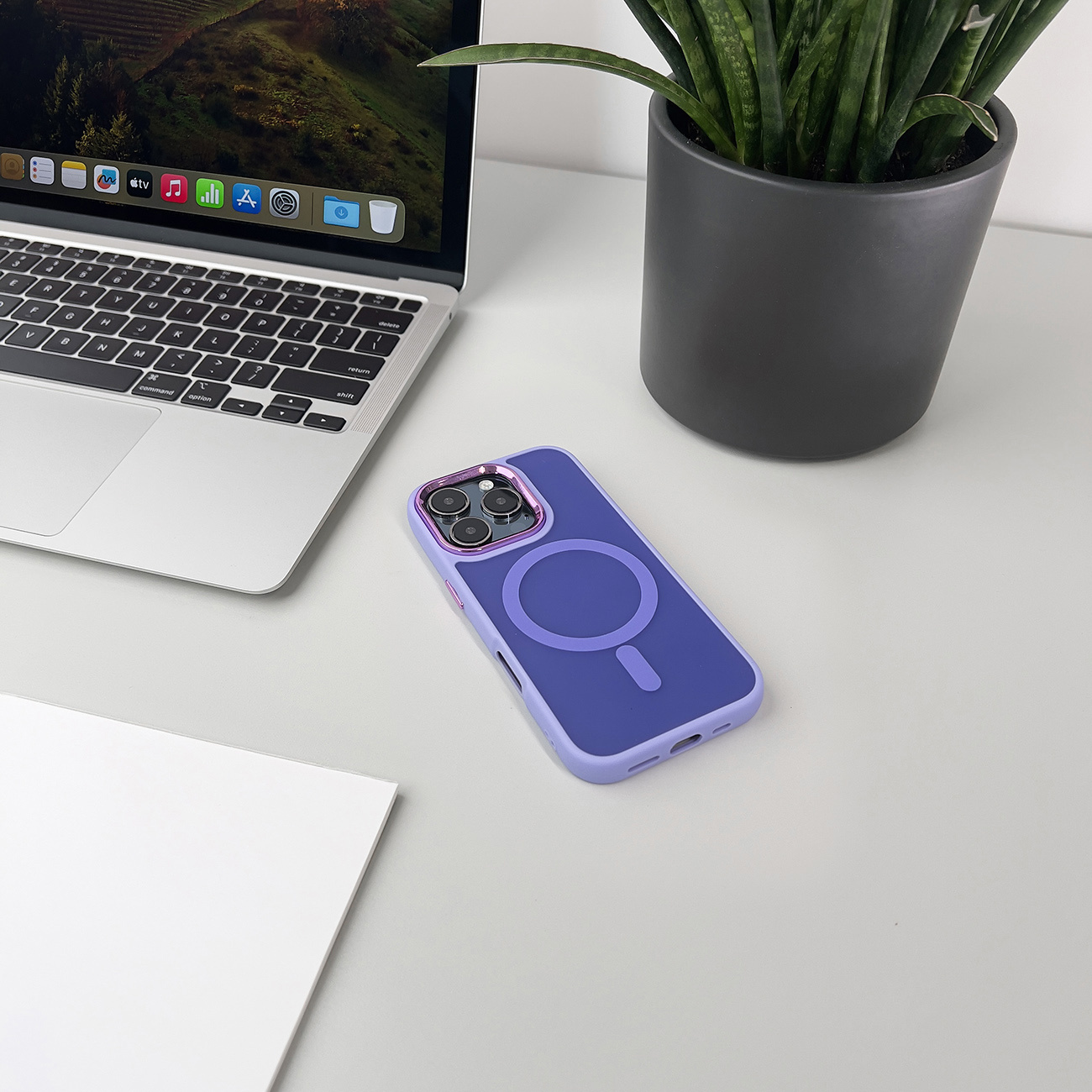 Fioletowe etui na telefon na biurku z laptopem i rośliną w tle.