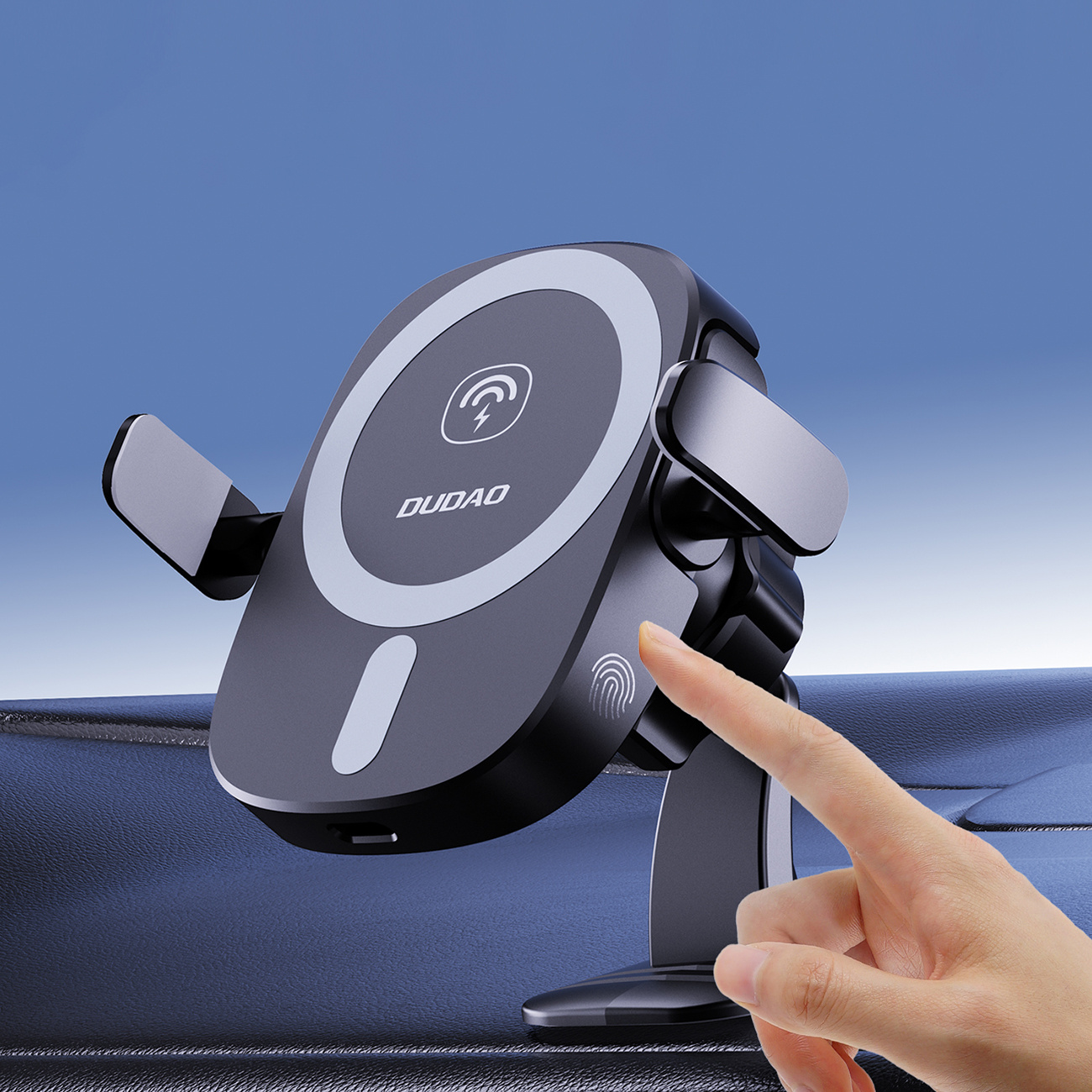 Ręka wskazuje na uchwyt na telefon na desce rozdzielczej samochodu. Uchwyt ma logo ładowania. Tło niebieskiego nieba.