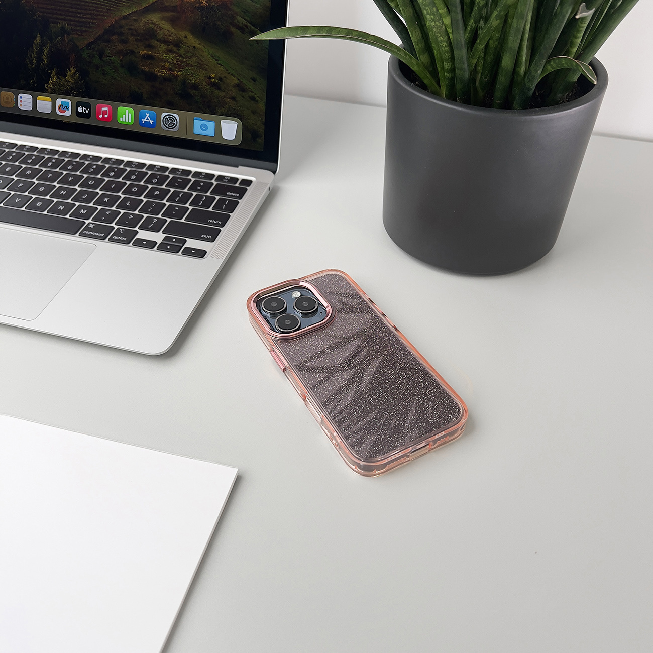 Telefon w etui na biurku, z laptopem i rośliną.