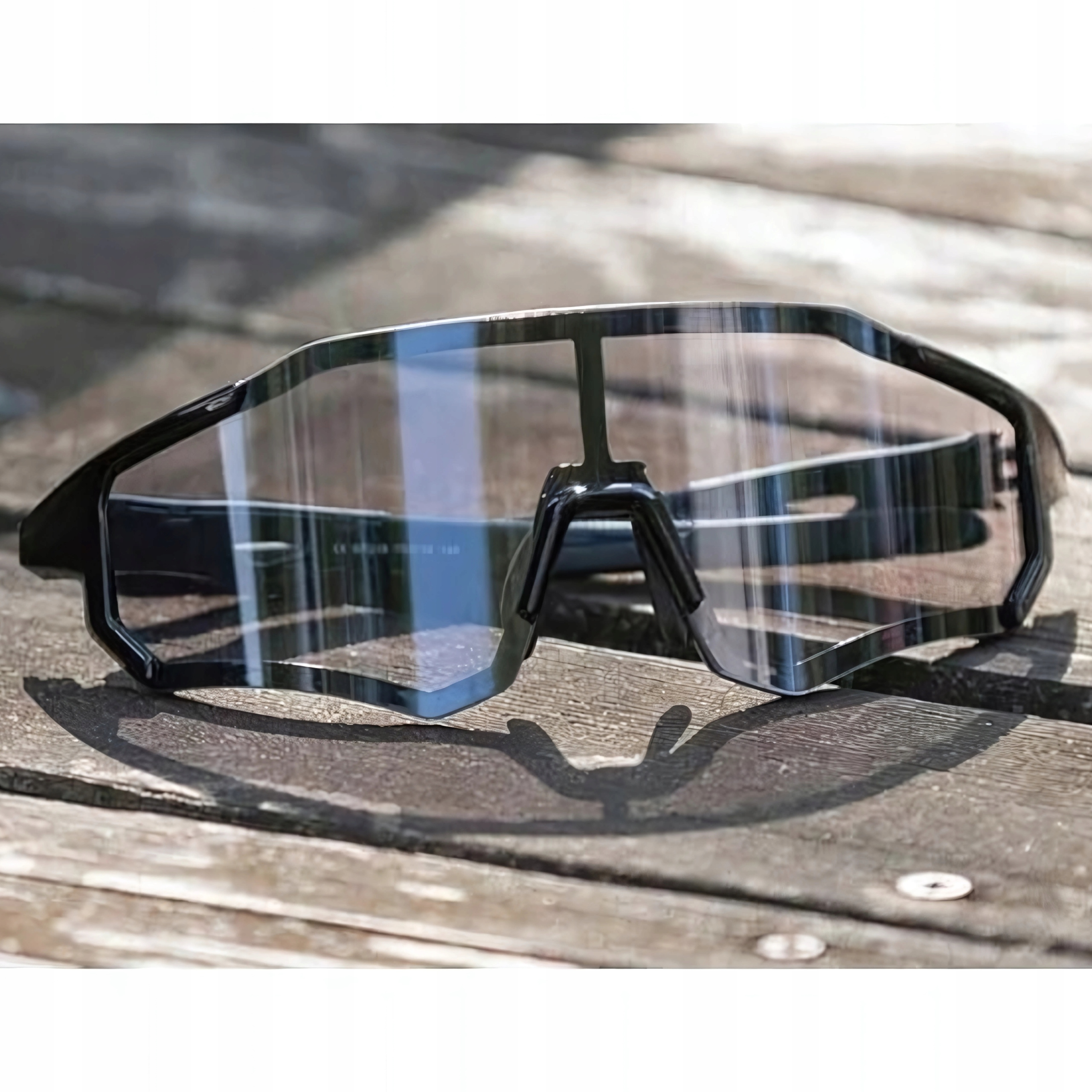 Czarne okulary przeciwsłoneczne na drewnianej powierzchni, z przezroczystymi soczewkami. Oprawka jest gruba i kanciasta.