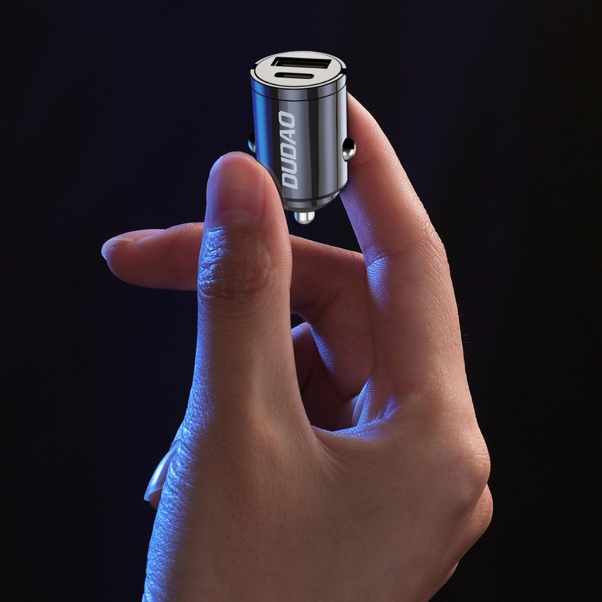 Dłoń trzyma czarną ładowarkę samochodową firmy DUDAO. Ładowarka ma dwa porty USB.