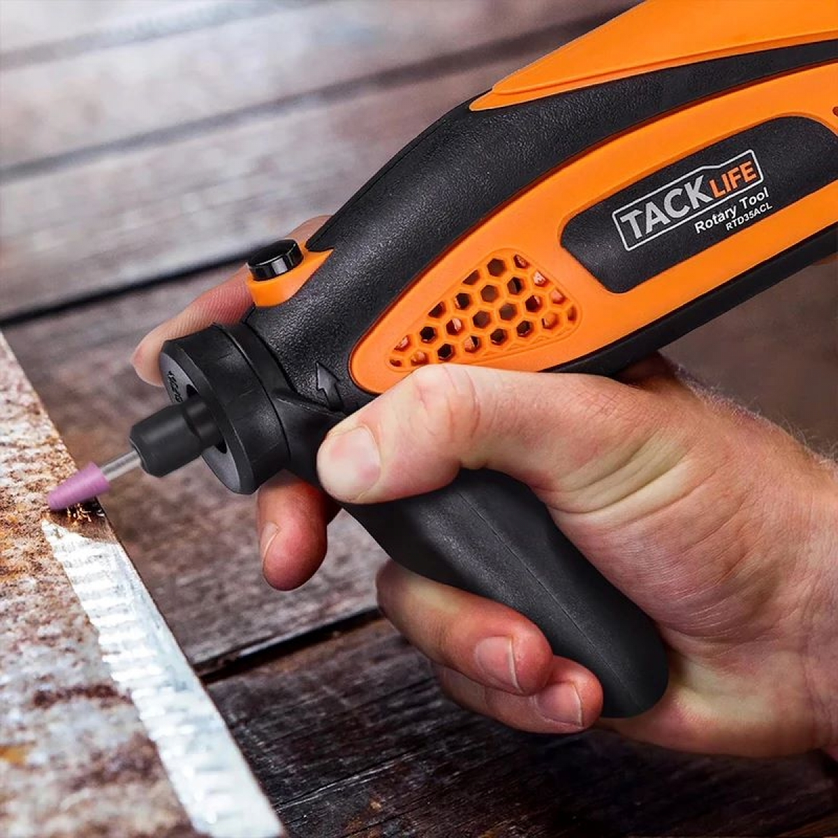 Una mano sosteniendo una herramienta rotativa naranja, trabajando en madera.