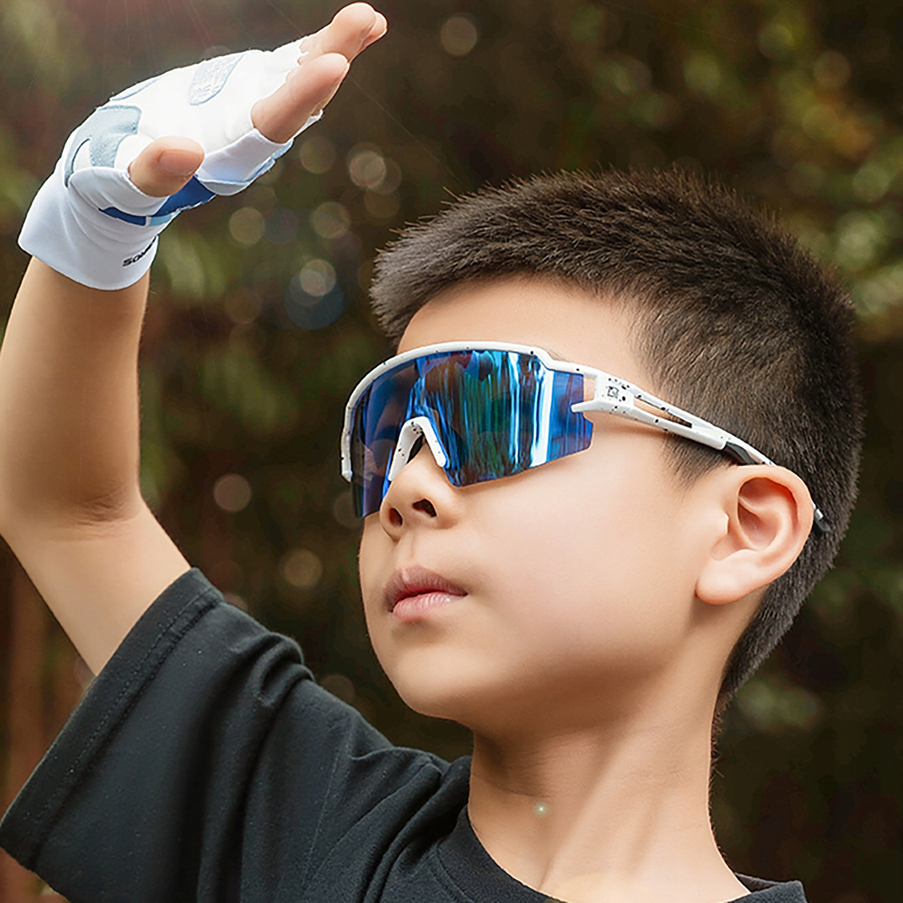 Ein Junge mit Sonnenbrille, schützt seine Augen mit der Hand, mit verschwommenem Hintergrund.