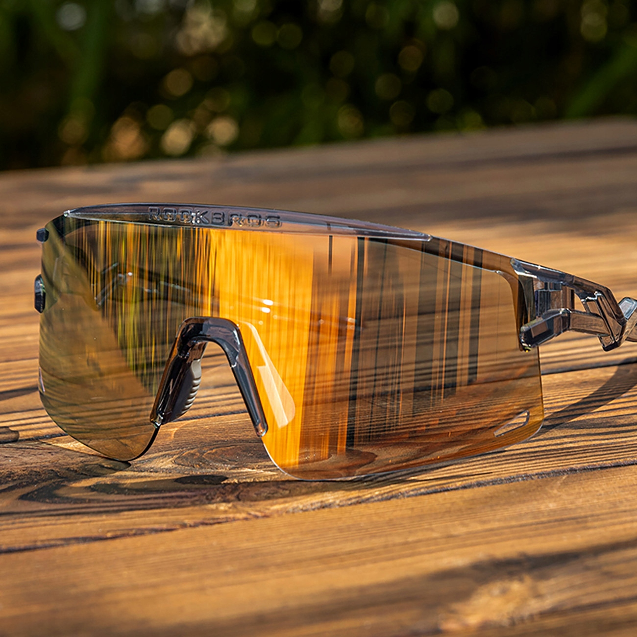 Sportsonnenbrille mit orangefarbenen Gläsern vor einem Holzgrund. Die Gläser spiegeln eine Landschaft wider.