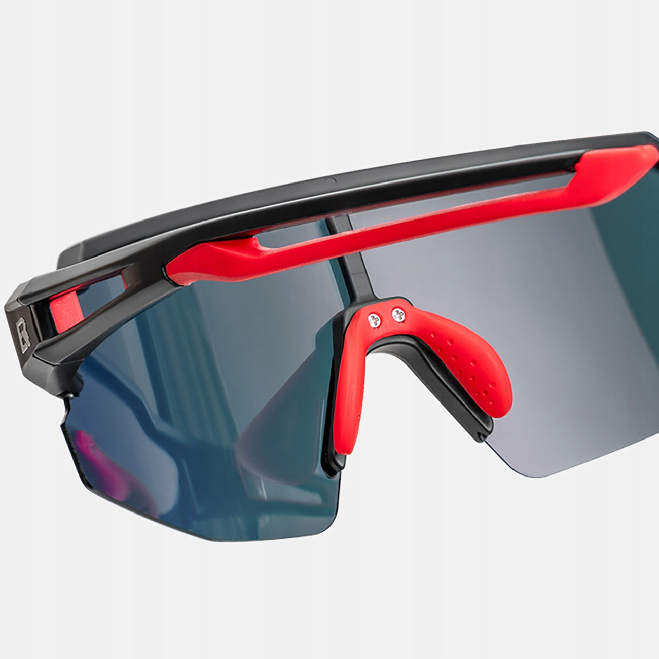 Nahaufnahme einer schwarzen und roten Sportsonnenbrille. Die Gläser sind dunkel. Die Brille steht vor weißem Hintergrund.
