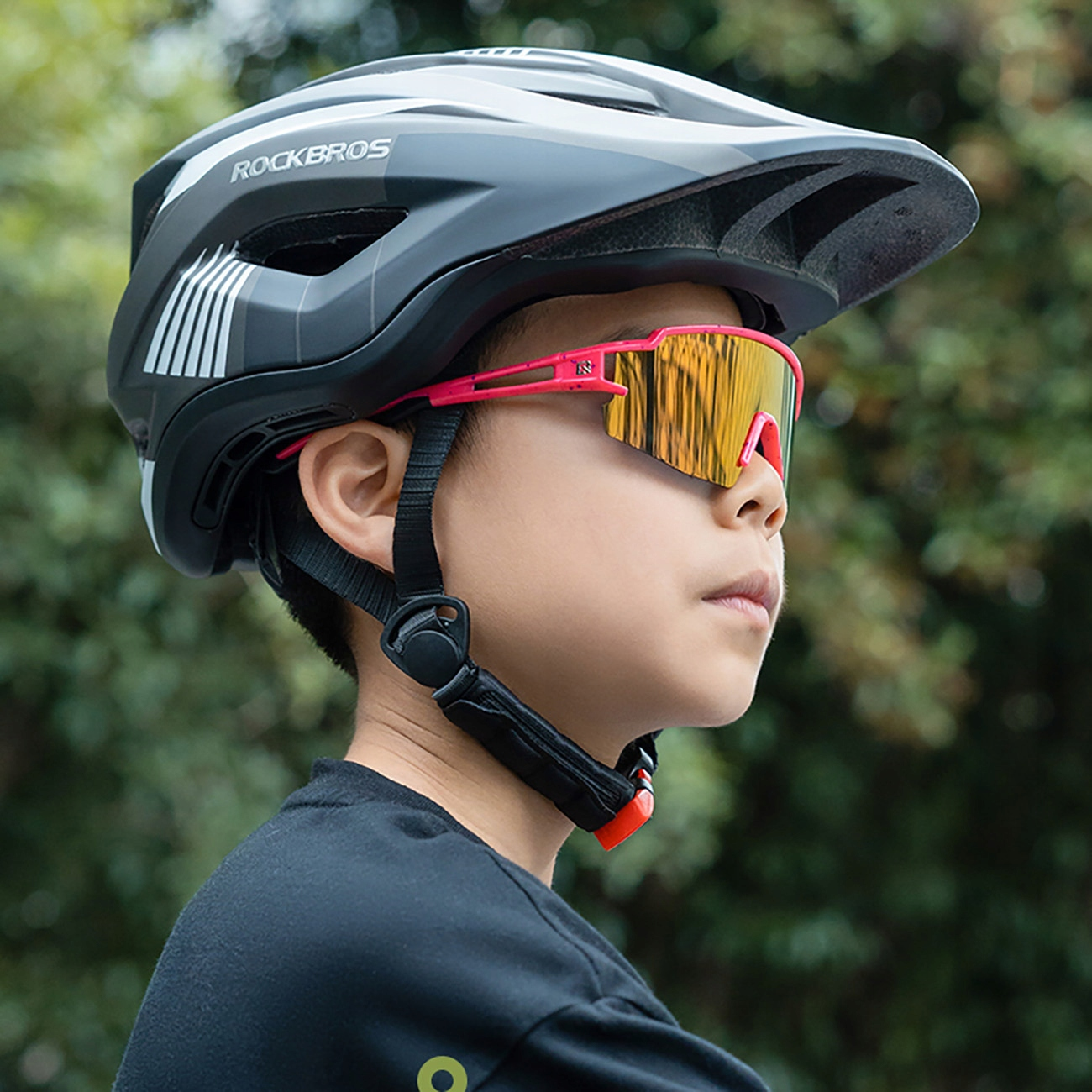 Ein Kind trägt einen Rockbros-Helm und eine pinkfarbene und gelbe Sportsonnenbrille. Das Kind schaut zur Seite.