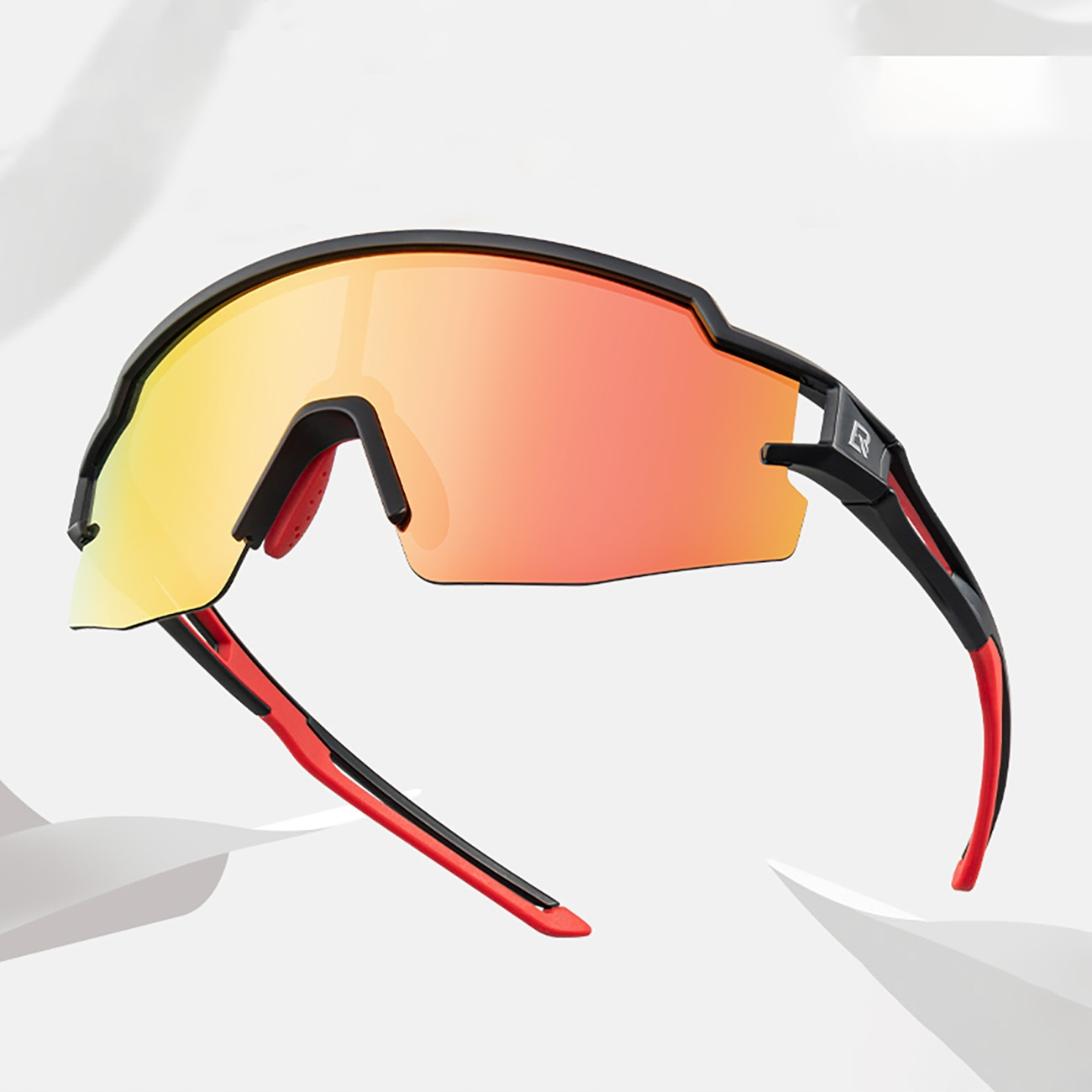 Schwarze und rote Sportsonnenbrille. Orangefarbene Gläser und schwarze Bügel. Die Brille liegt auf weißem Untergrund.
