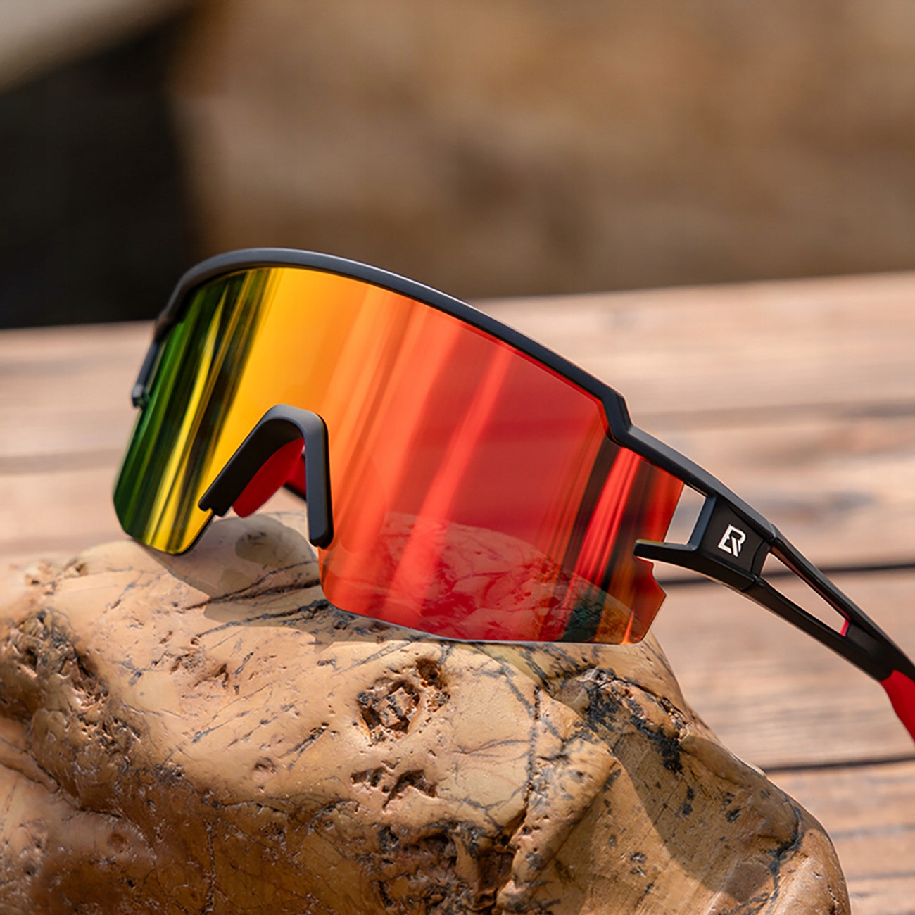 Schwarze und rote Sportsonnenbrille auf einem Stein. Die Gläser sind reflektierend und haben eine Farbverlauf.