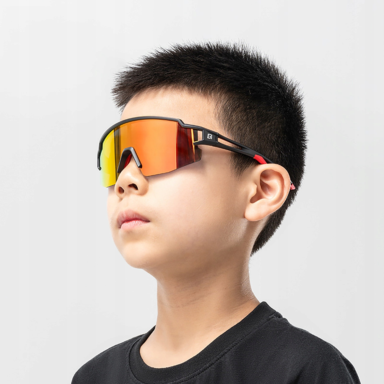 Ein Junge mit Sportsonnenbrille mit rot-orange getönten Gläsern, schwarzem Rahmen und schwarzem Hemd.