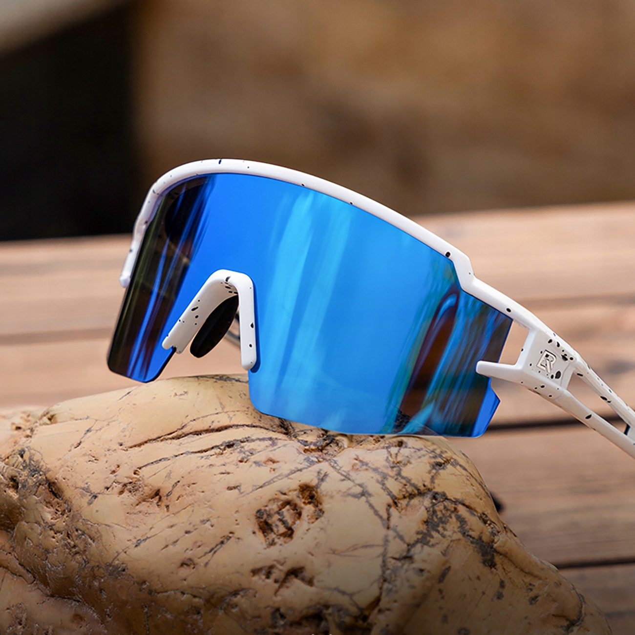 Occhiali da sole sportivi bianchi con lenti blu su una roccia. Gli occhiali hanno un motivo bianco e nero.
