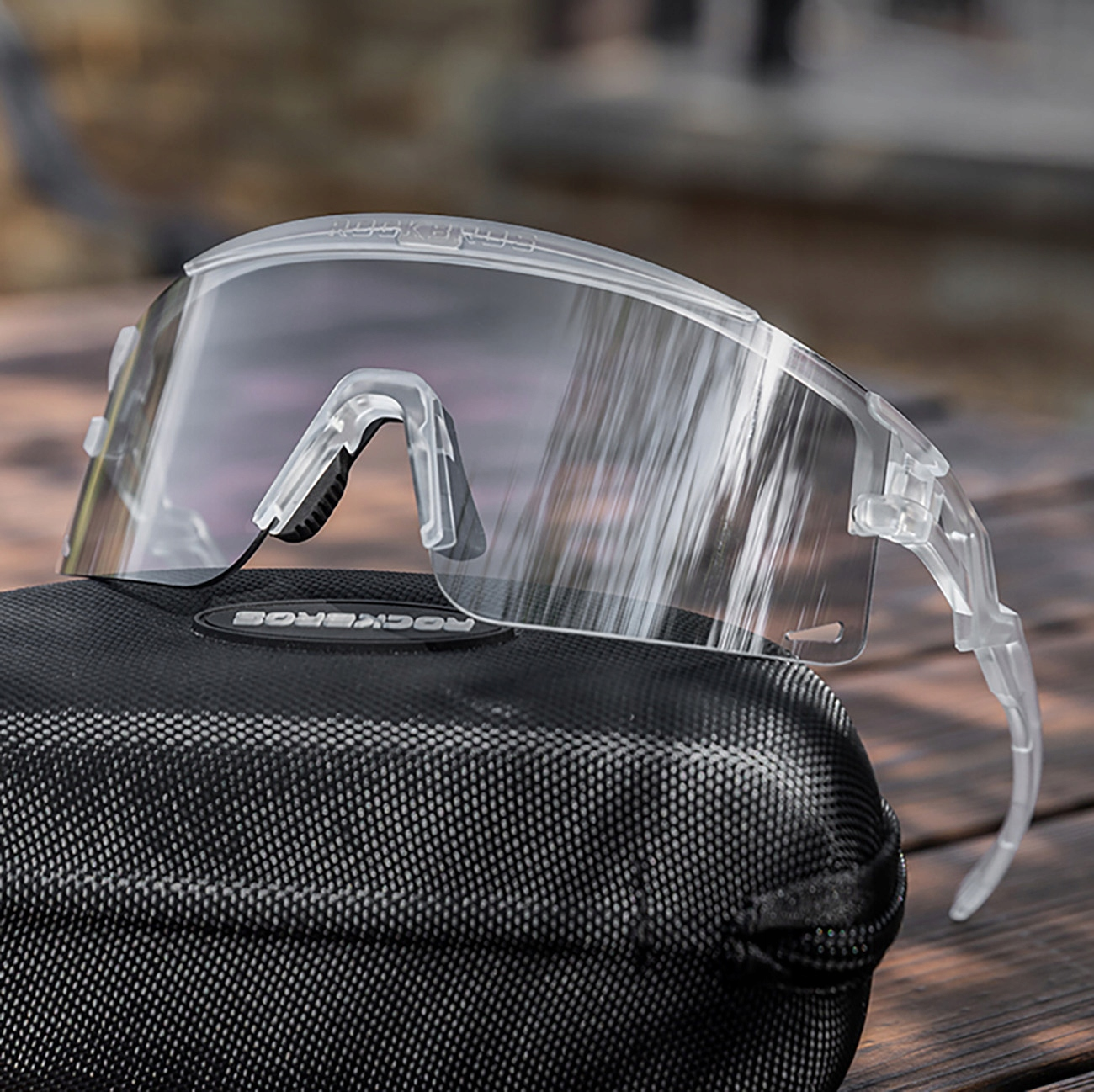 Nahaufnahme einer Radbrille in einem Etui. Die Brille ist transparent, das Etui schwarz. Holzoberfläche.