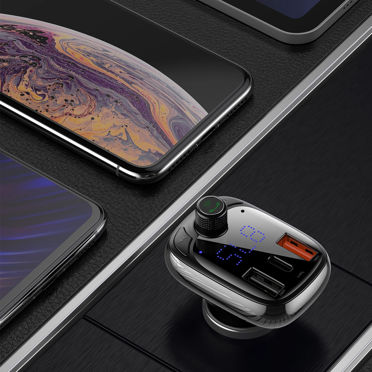 Ładowarka samochodowa z ekranem i portami USB. W pobliżu dwa telefony. Jeden to błyszczący smartfon.