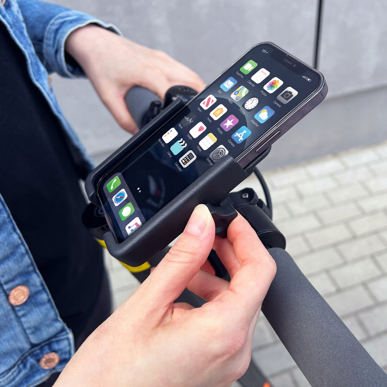 Eine Person hält ein Telefon in einer Autotelefonhalterung an einem Rollerlenker. Das Telefon zeigt App-Symbole.