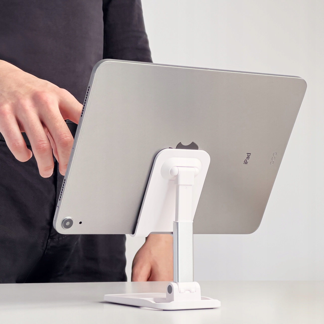 Osoba trzymająca iPada na białym, regulowanym stojaku, z widoczną tylną częścią iPada.
