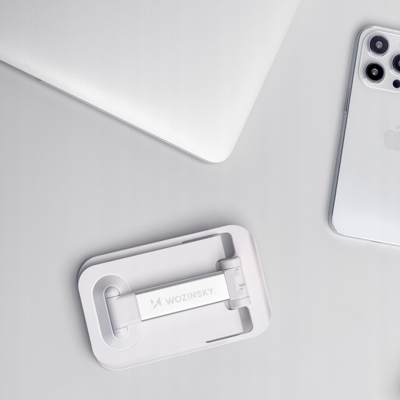 Biały, składany stojak na telefon z laptopem i telefonem na białej powierzchni.