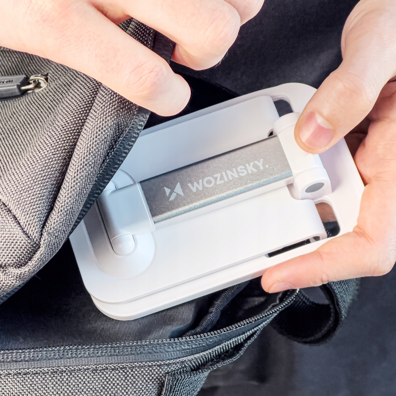 Ręce wkładające biały stojak na telefon do czarnego plecaka.