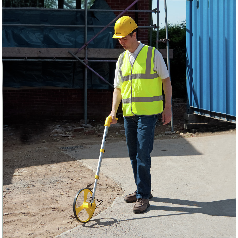 Eine Person in gelber Weste und Helm benutzt ein Stanley-Messrad auf einer Baustelle.