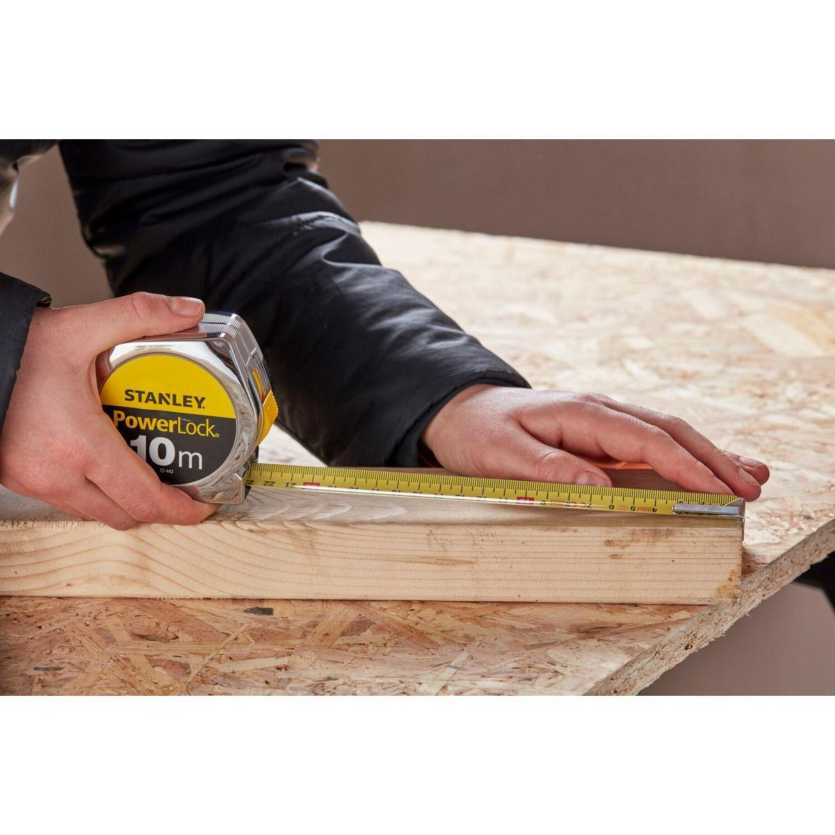 Eine Person, die ein Stanley PowerLock 10m Maßband auf Holz verwendet.